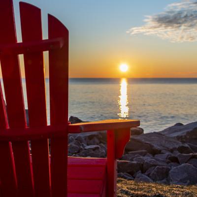 一张红色的阿迪朗达克椅子，面对着日出时的湖面.